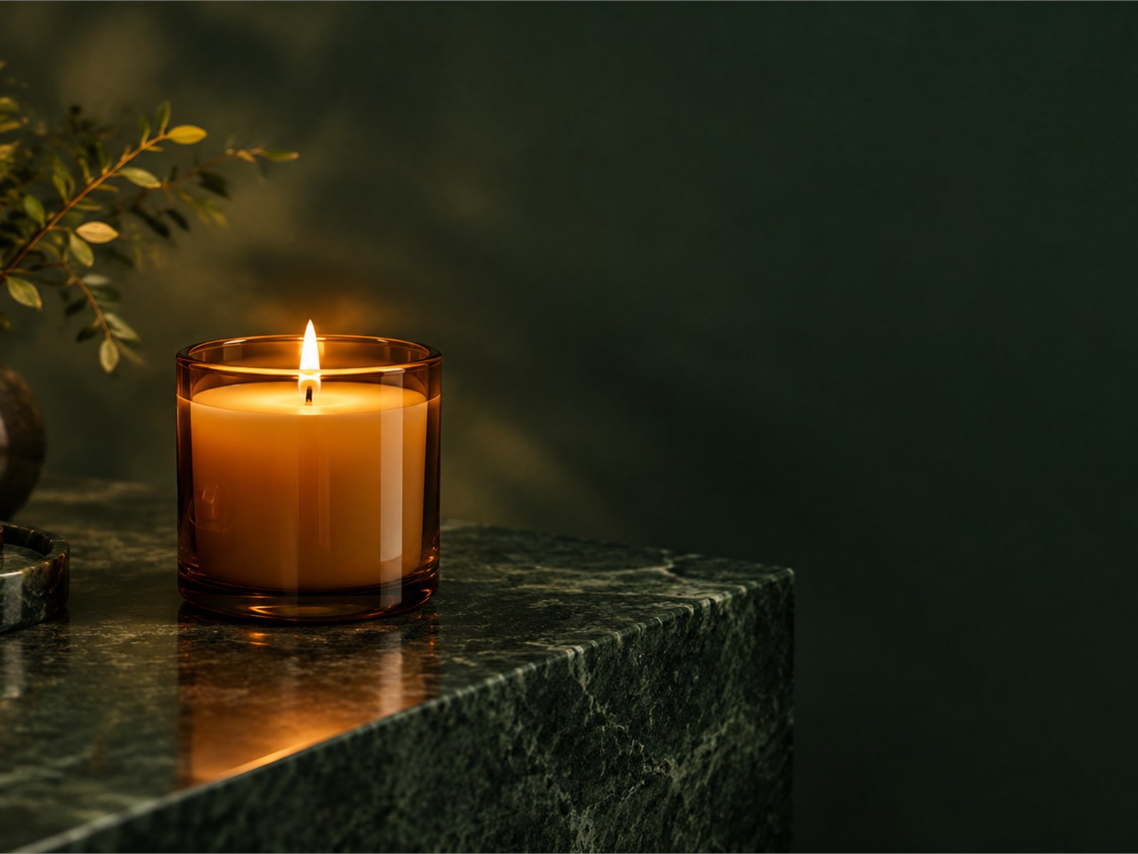 A lit candle in an amber glass vessel on a dark wooden table, late in the evening